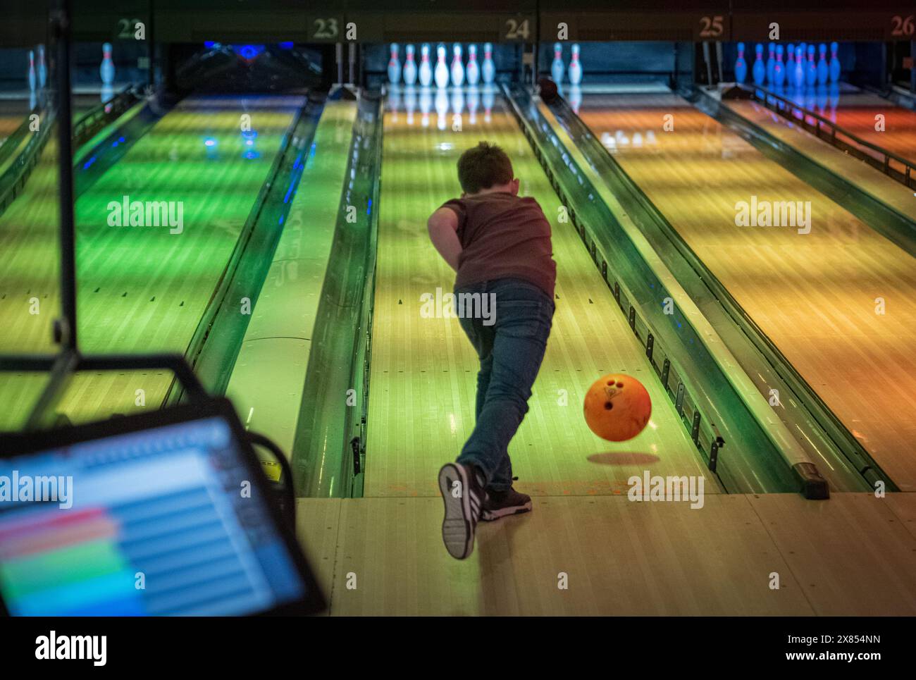 Enfant prenant son meilleur tir dans le bowling, Bowler lance une balle orange sous des lumières vibrantes, une action dynamique dans un bowling coloré et moderne Banque D'Images