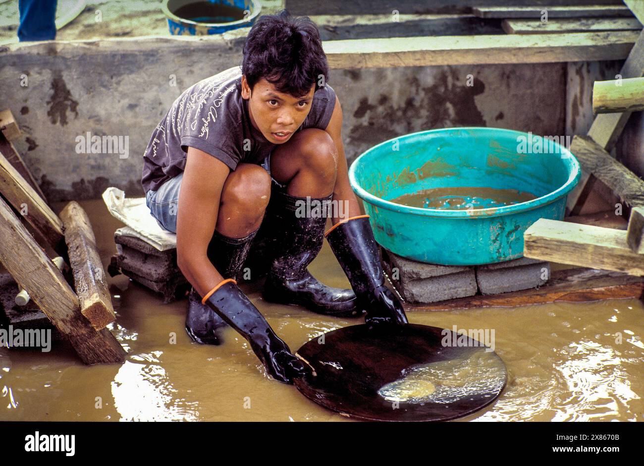 Philippines, Mindenao, lac Sebu ; un travailleur de l'industrie des mines d'or tamise avec du mercure l'eau boueuse à la recherche d'or. Banque D'Images