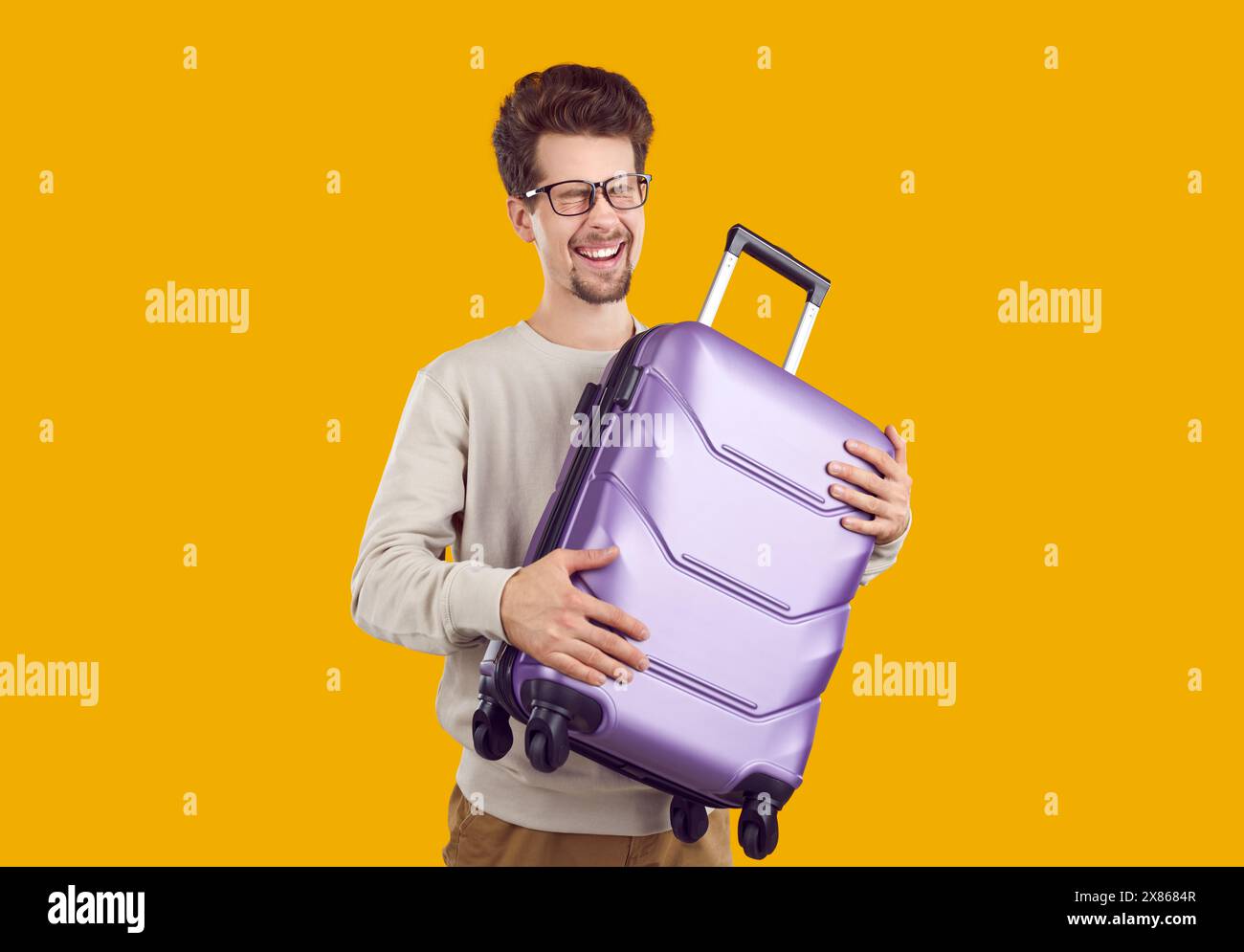 Portrait d'un jeune homme heureux qui rit joyeusement tenant une petite valise de voyage dans ses mains. Banque D'Images