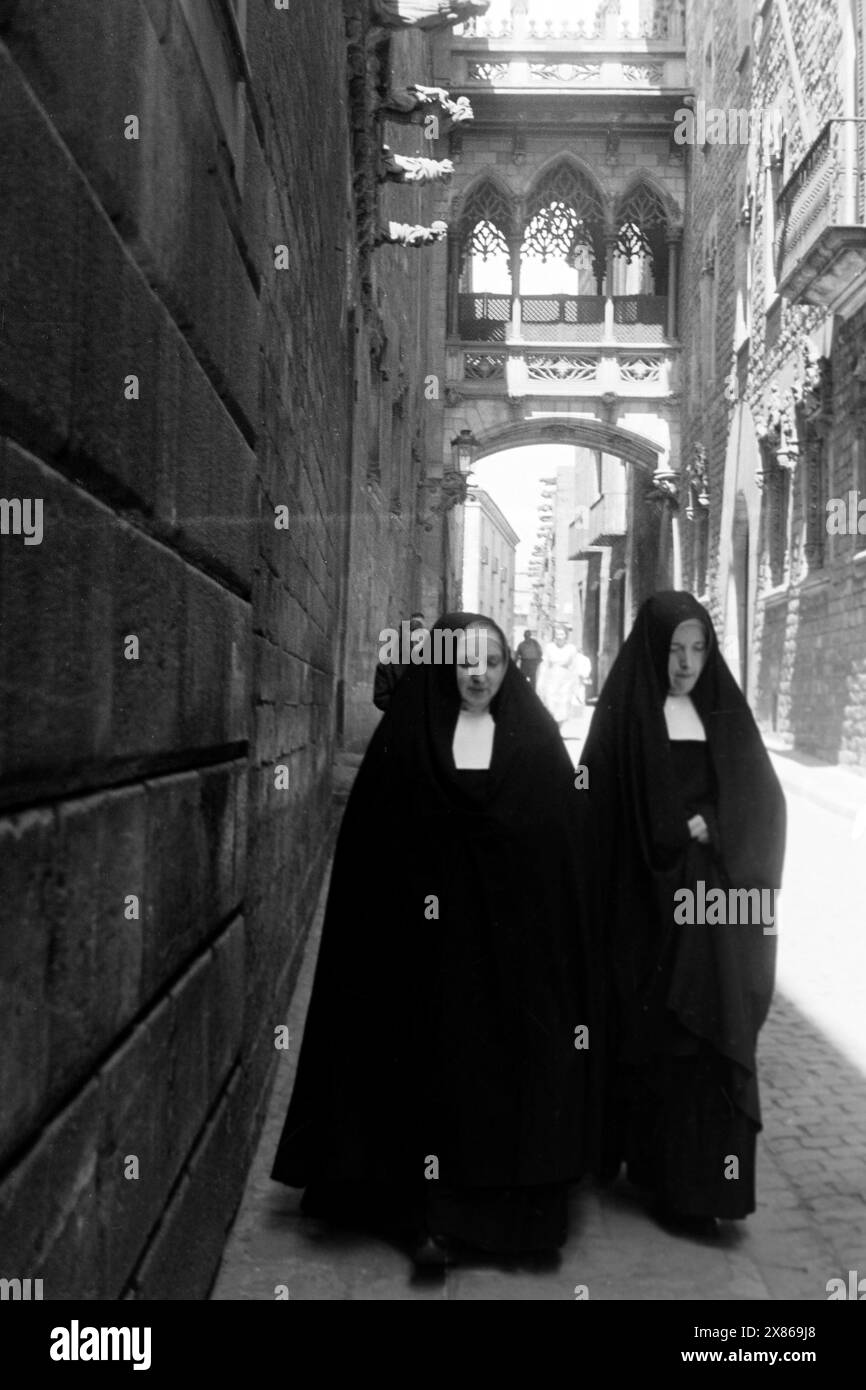 Zwei Ordensschwestern in der Calle del Obispo in der Altstadt von Barcelona, im Hintergrund die neugotische Brücke, die die Casa de los Canónigos mit der Generalitat von Katalonien verbindet, Spanien 1957. Deux religieuses dans la Calle del Obispo dans le centre historique de Barcelone, en arrière-plan le pont néo-gothique reliant la Casa de los Canónigos à la Generalitat de Catalogne, Espagne 1957. Banque D'Images