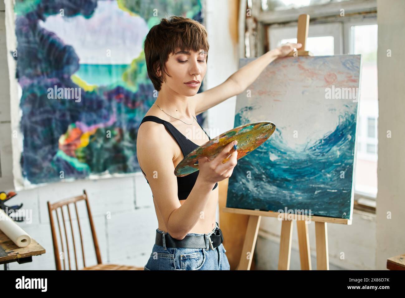 Une femme peint un tableau avec un pinceau à la main. Banque D'Images