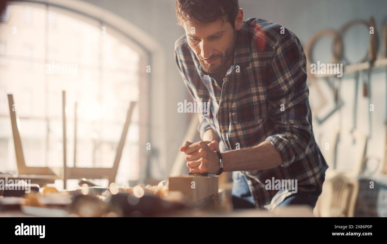 Talentueux jeune artisan artisan dans la chemise à carreaux utilisant l'avion de main pour former une barre de bois. Attrayant Carpenter est satisfait des résultats. Homme travaillant sur un projet dans un Loft Studio avec des outils sur des murs. Banque D'Images