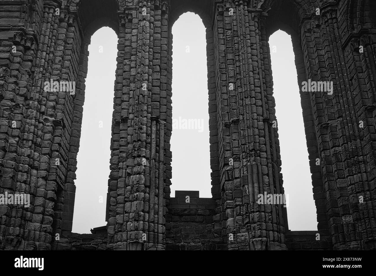 Photo en noir et blanc d'anciennes colonnes de pierre avec des ouvertures voûtées, partie d'une ruine historique. Banque D'Images