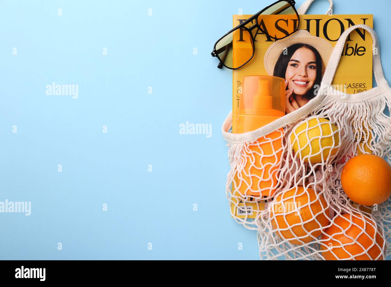 Sac à ficelle avec magazine, fruits et accessoires d'été sur fond bleu clair, pose plate. Espace pour le texte Banque D'Images