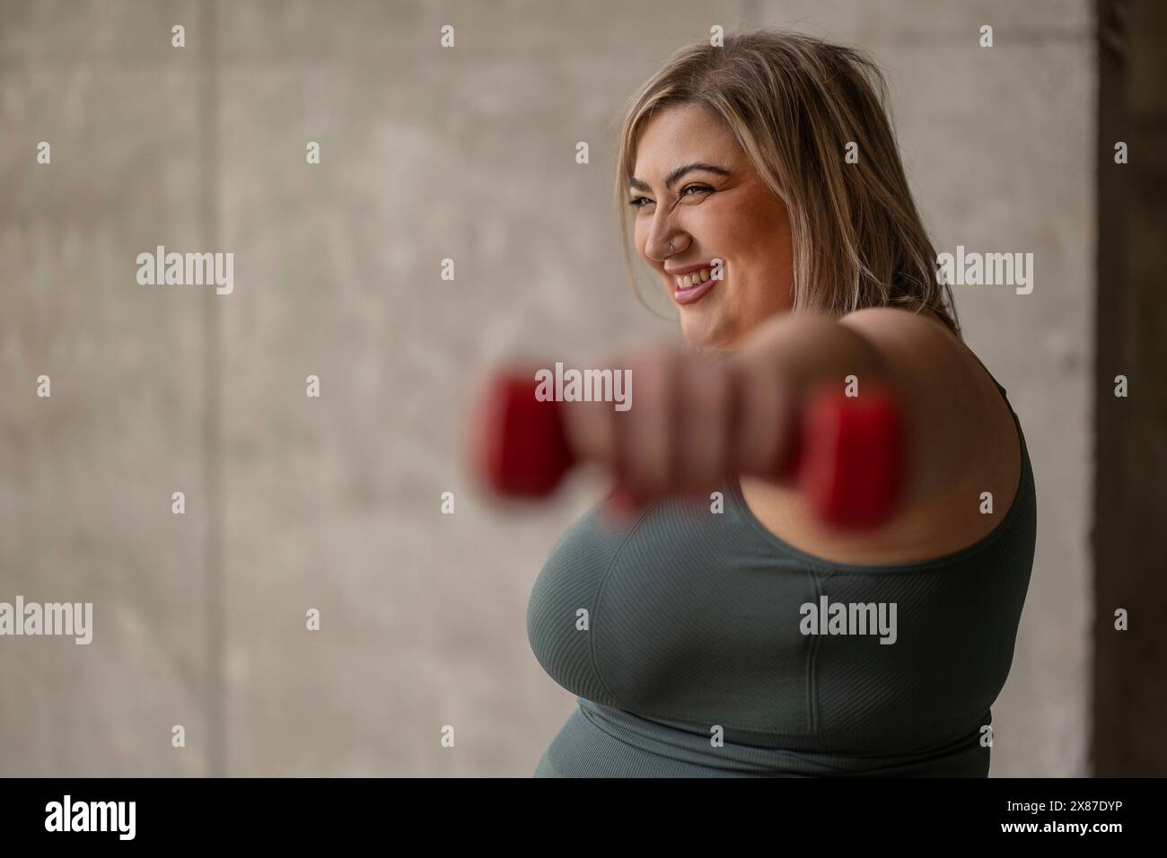 Femme sinueuse heureuse exerçant avec haltère près du mur Banque D'Images