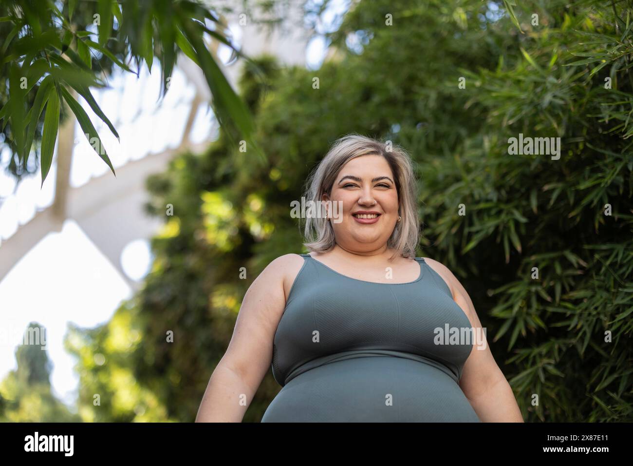 Heureuse femme sinueuse debout près des plantes dans le parc Banque D'Images