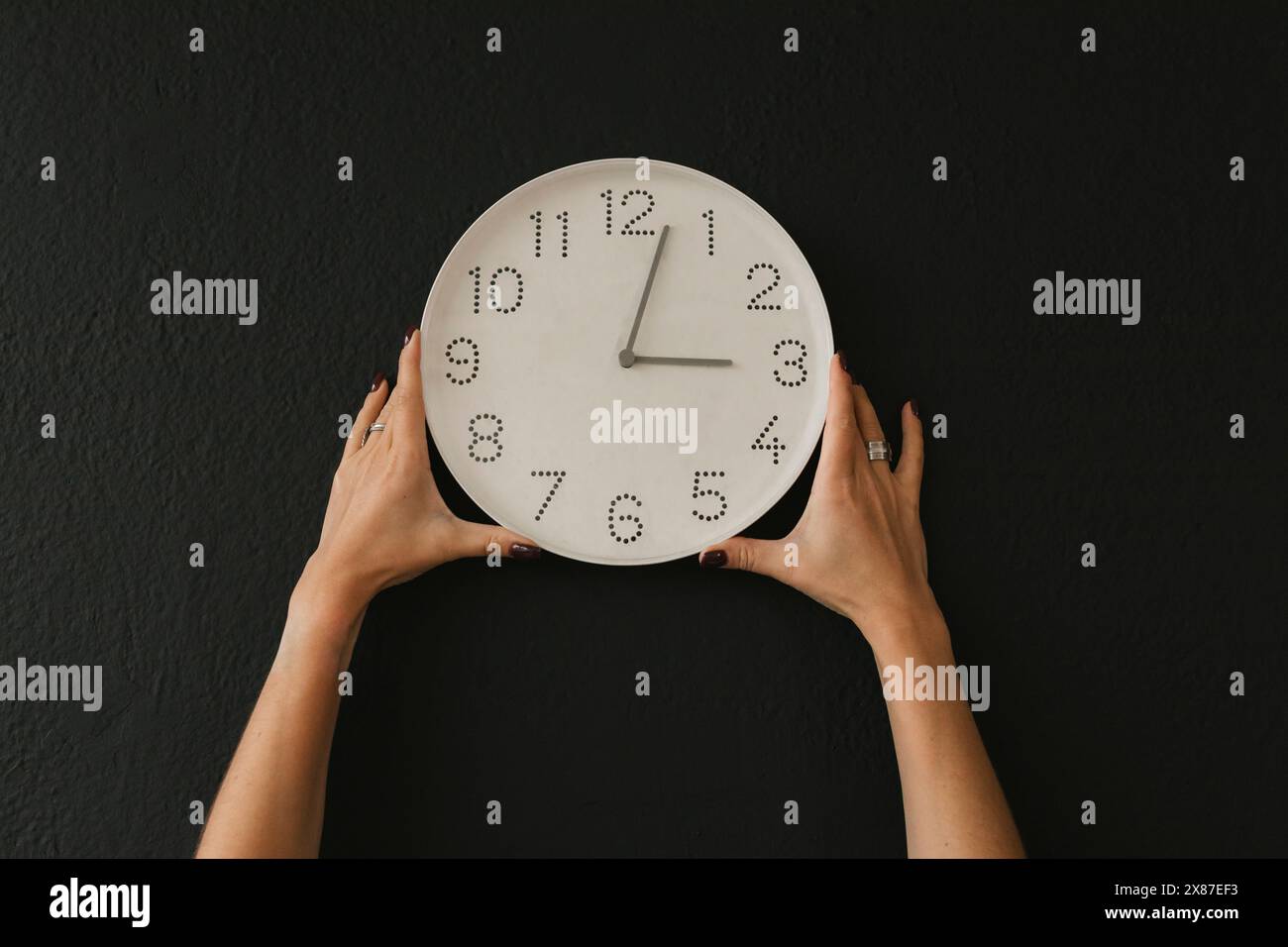 Mains de la femme tenant l'horloge murale sur fond noir Banque D'Images