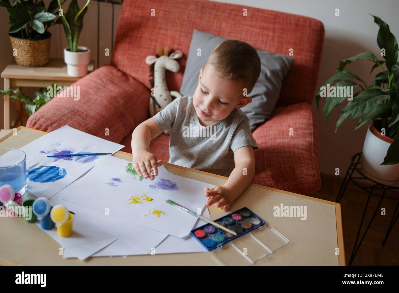 Garçon faisant des empreintes de mains sur une feuille de papier à la maison Banque D'Images