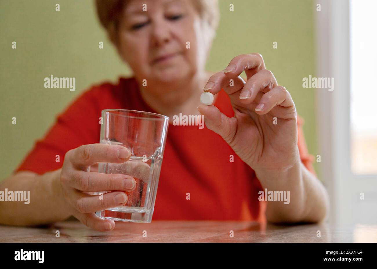 Femme âgée tenant verre d'eau et pilule à la maison Banque D'Images