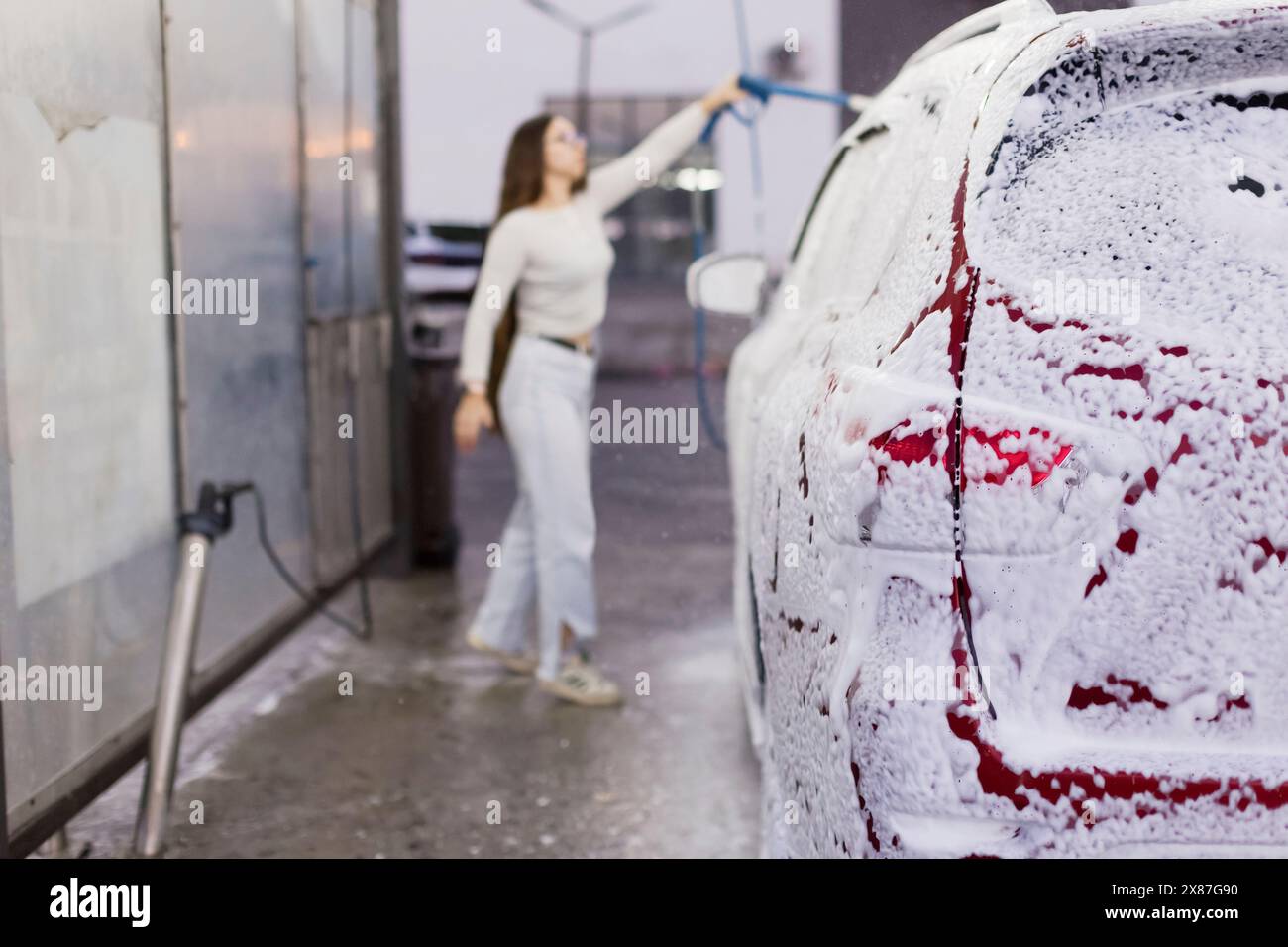 Femme utilisant l'eau à haute pression et la voiture de nettoyage au garage Banque D'Images