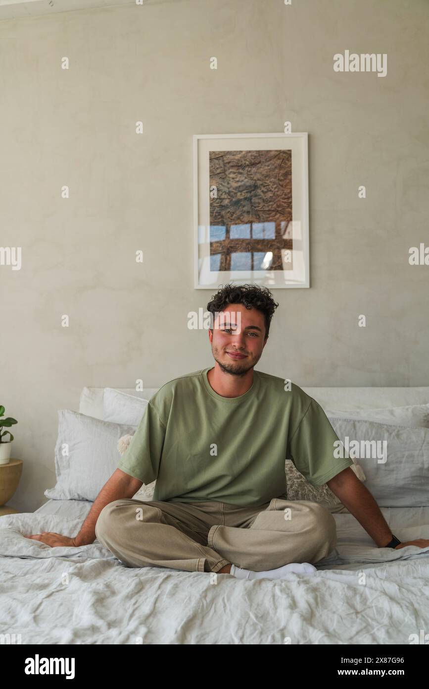 Homme souriant assis sur le lit à la maison Banque D'Images