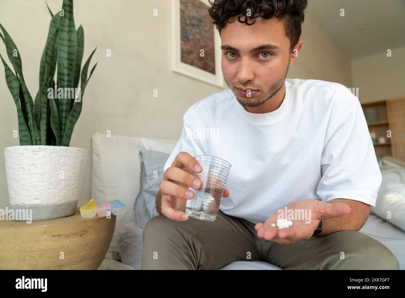 Jeune homme tenant des pilules et un verre d'eau sur le lit à la maison Banque D'Images
