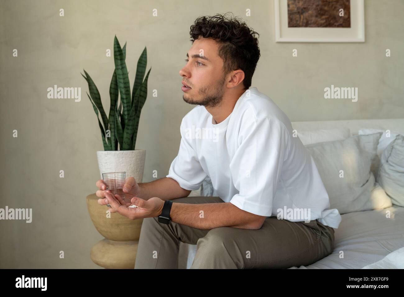 Jeune homme assis avec des médicaments et un verre d'eau sur le lit à la maison Banque D'Images