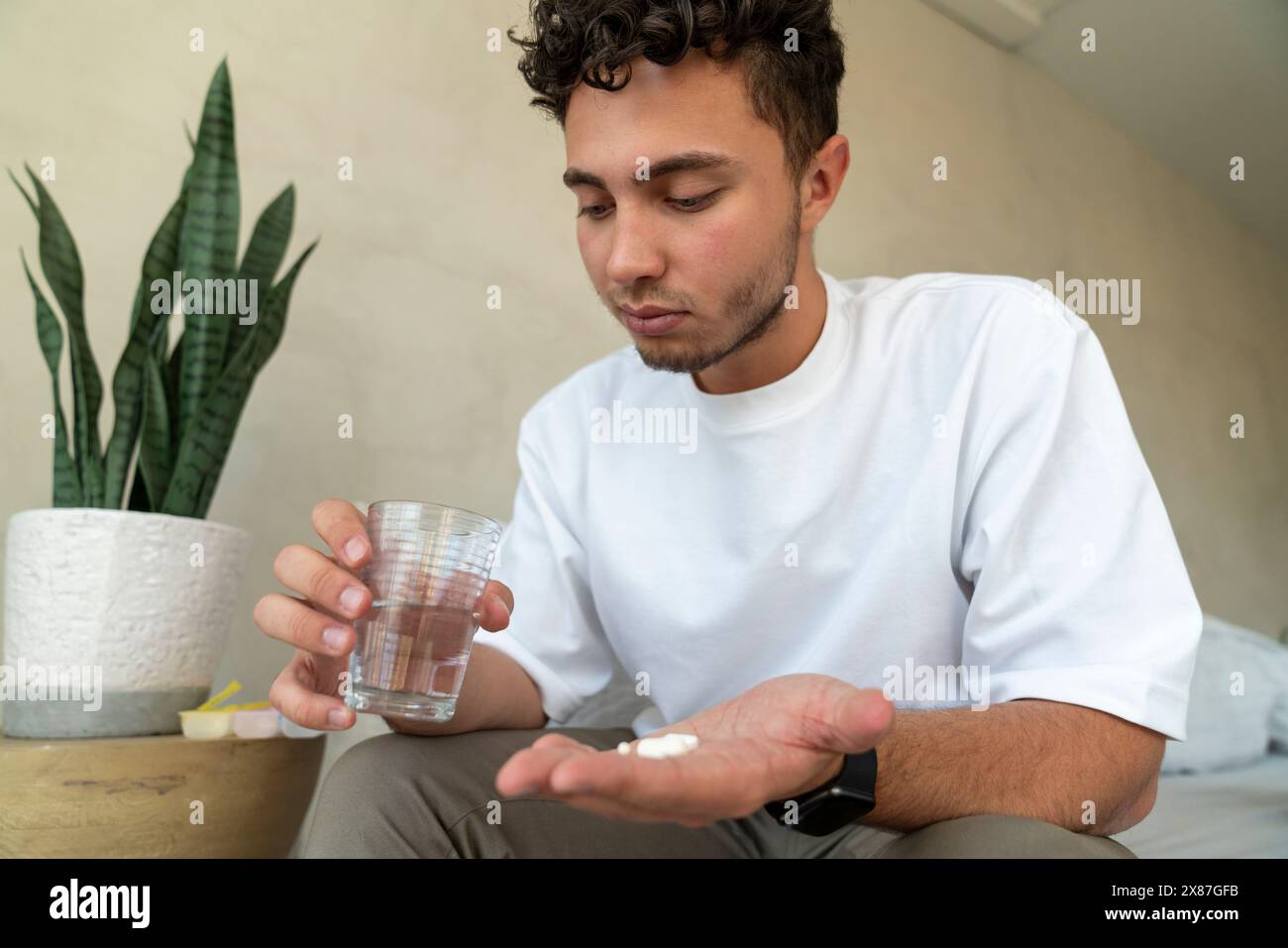 Homme assis avec des médicaments et un verre d'eau sur le lit à la maison Banque D'Images
