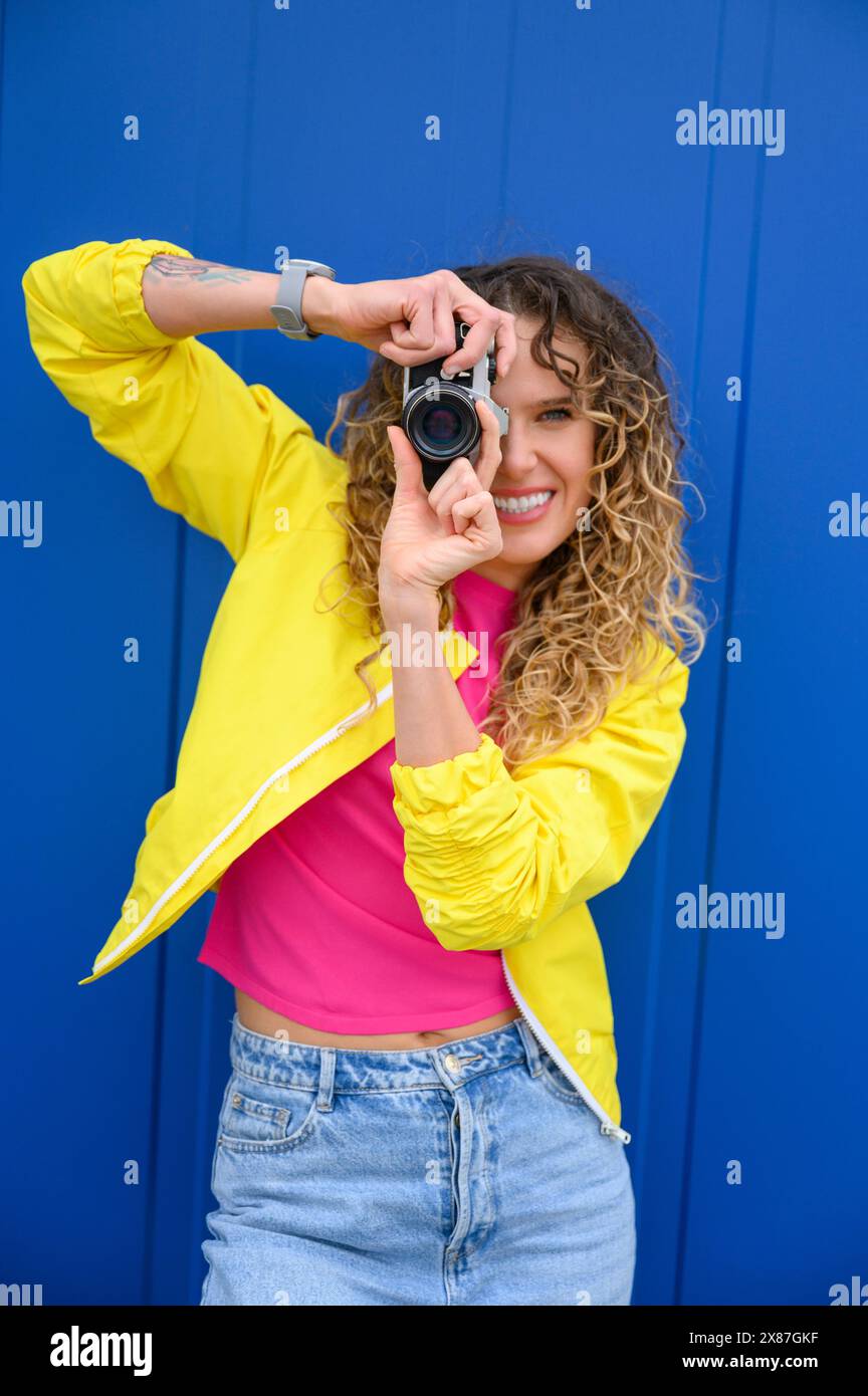 Femme souriante photographiant à travers la caméra devant le mur bleu Banque D'Images