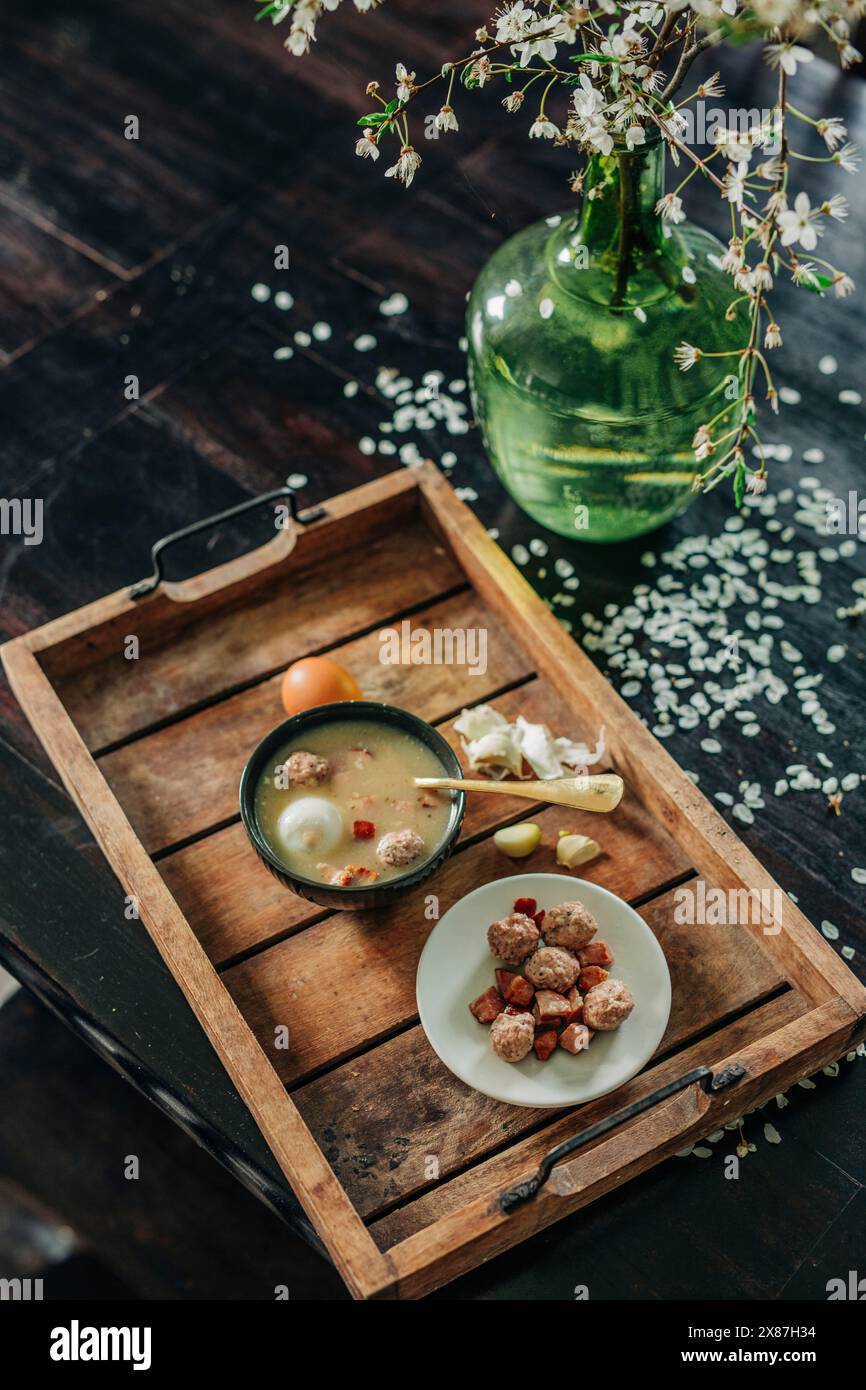 Soupe polonaise traditionnelle fraîche Zurek dans un bol sur plateau en bois par vase avec fleur Banque D'Images