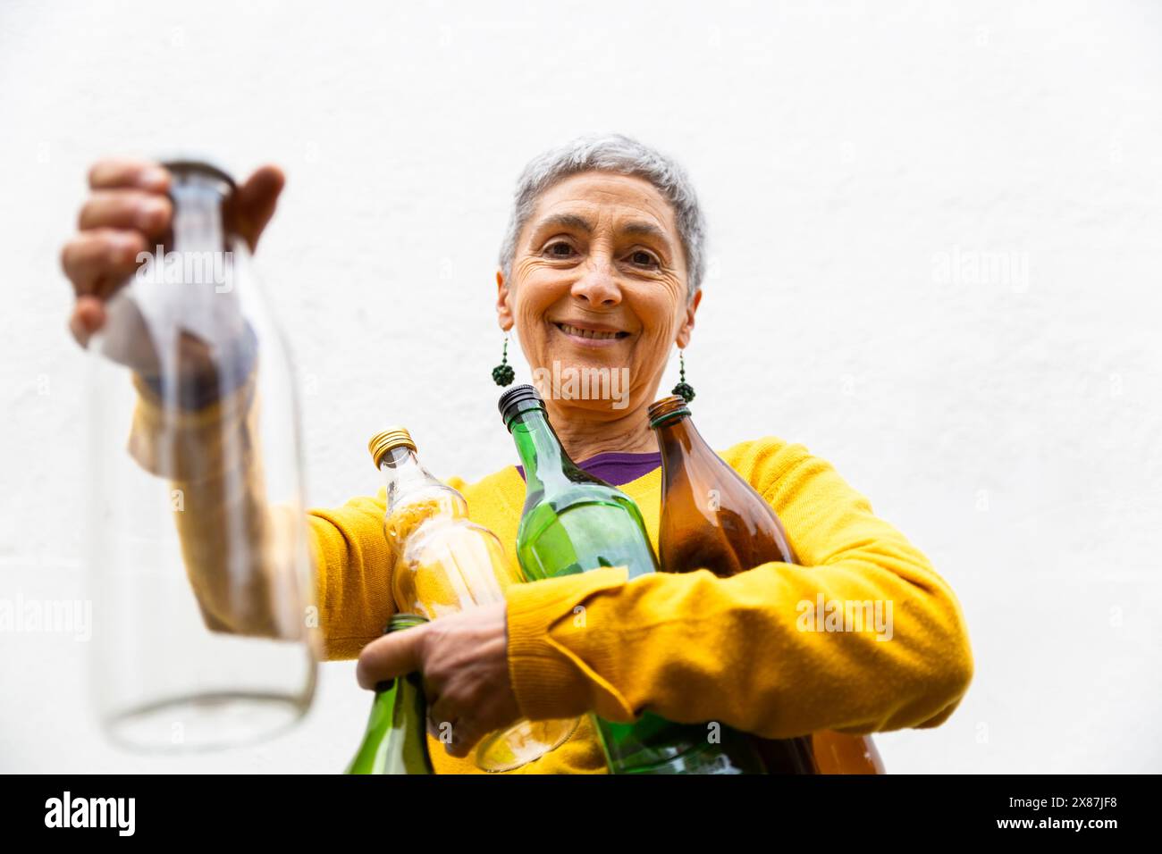 Femme âgée souriante recyclant des bouteilles en verre Banque D'Images