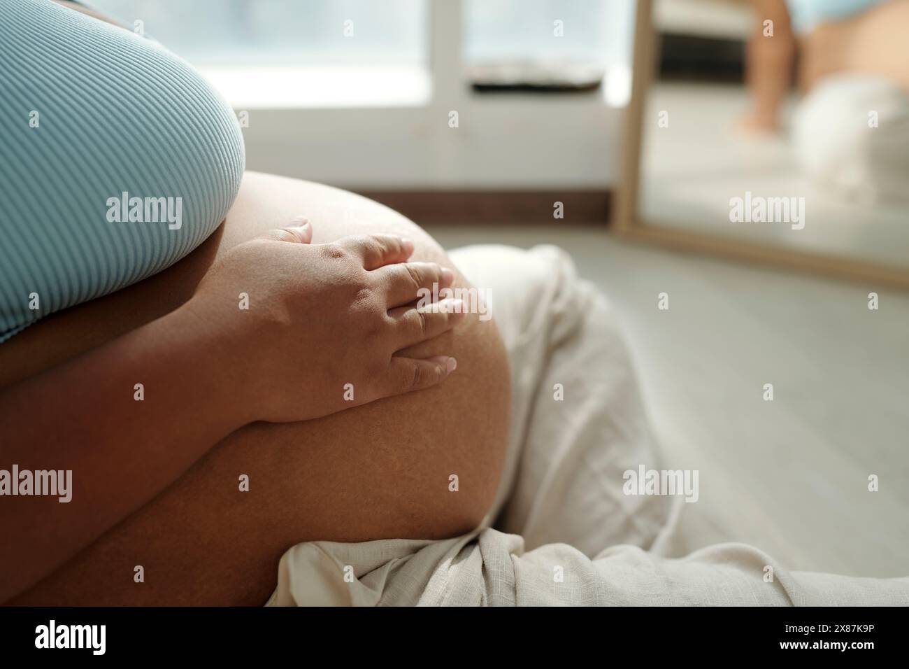 Femme enceinte de taille plus avec la main sur le ventre assis à la maison Banque D'Images Femme enceinte de taille plus avec la main sur le ventre assis à la maison Banque D'Images