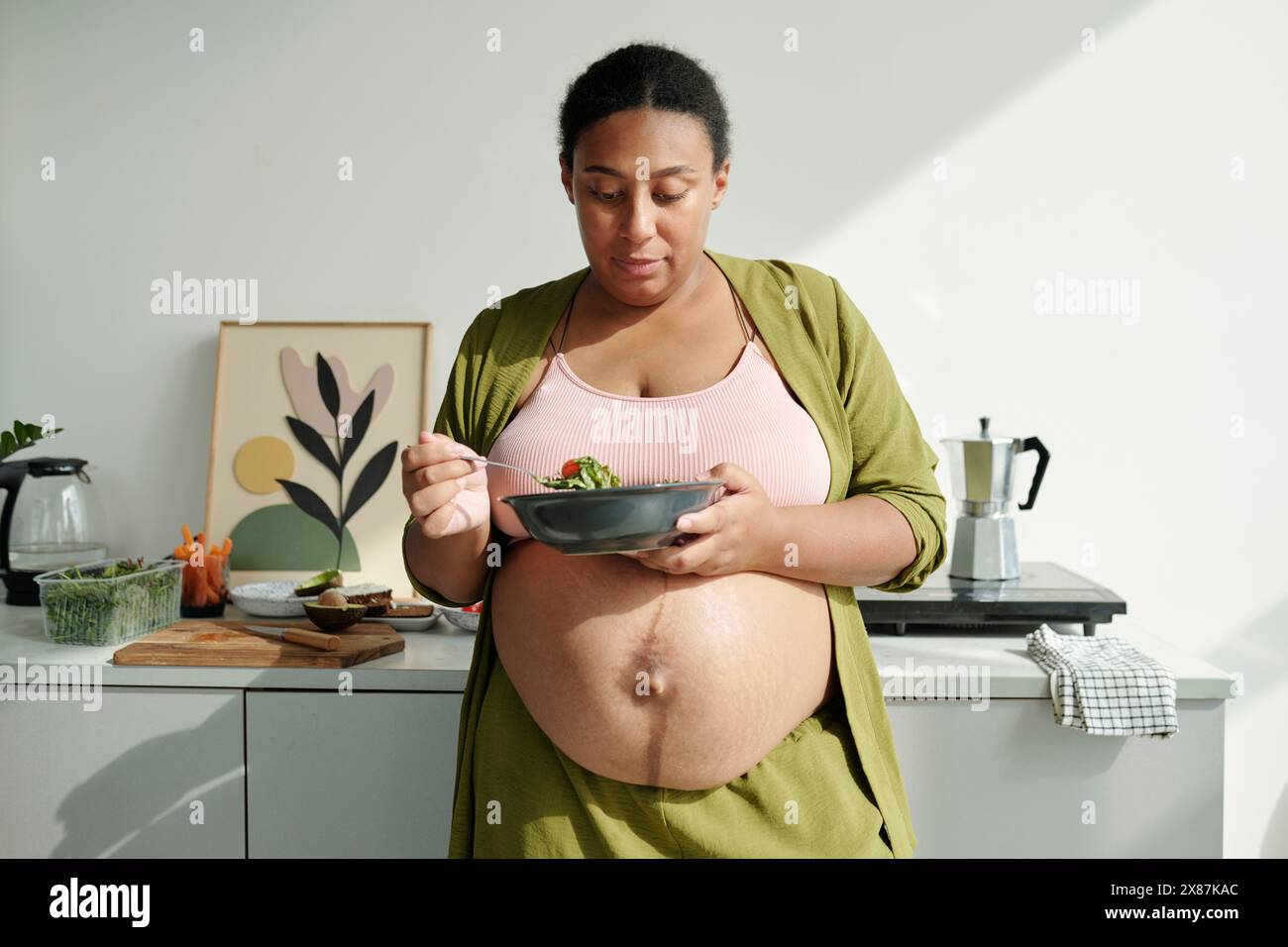 Femme enceinte de taille plus mangeant de la salade avec des légumes frais dans la cuisine à la maison Banque D'Images