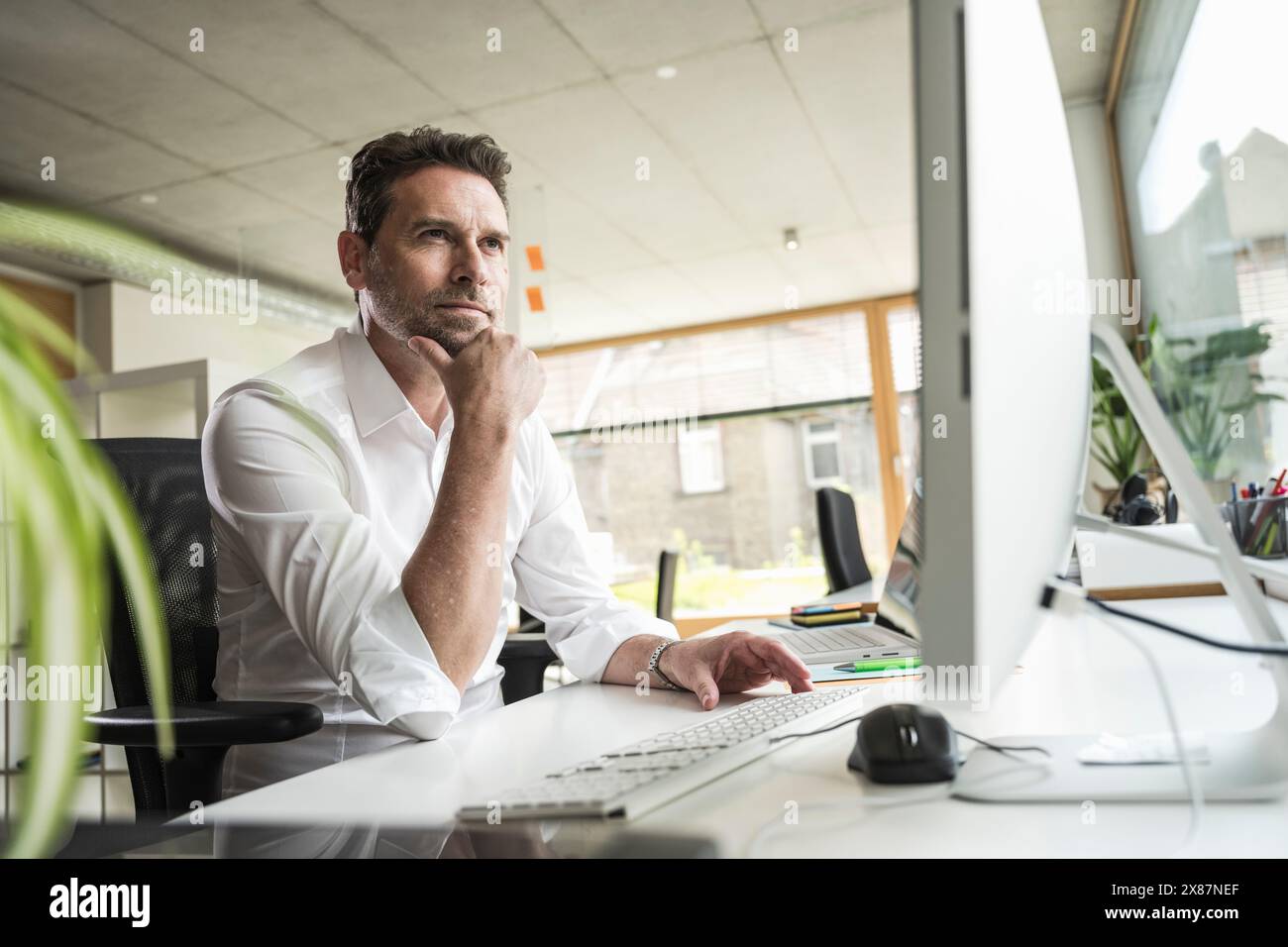 Homme d'affaires attentionné avec la main sur le menton assis au bureau de l'ordinateur dans le bureau Banque D'Images Homme d'affaires attentionné avec la main sur le menton assis au bureau de l'ordinateur dans le bureau Banque D'Images