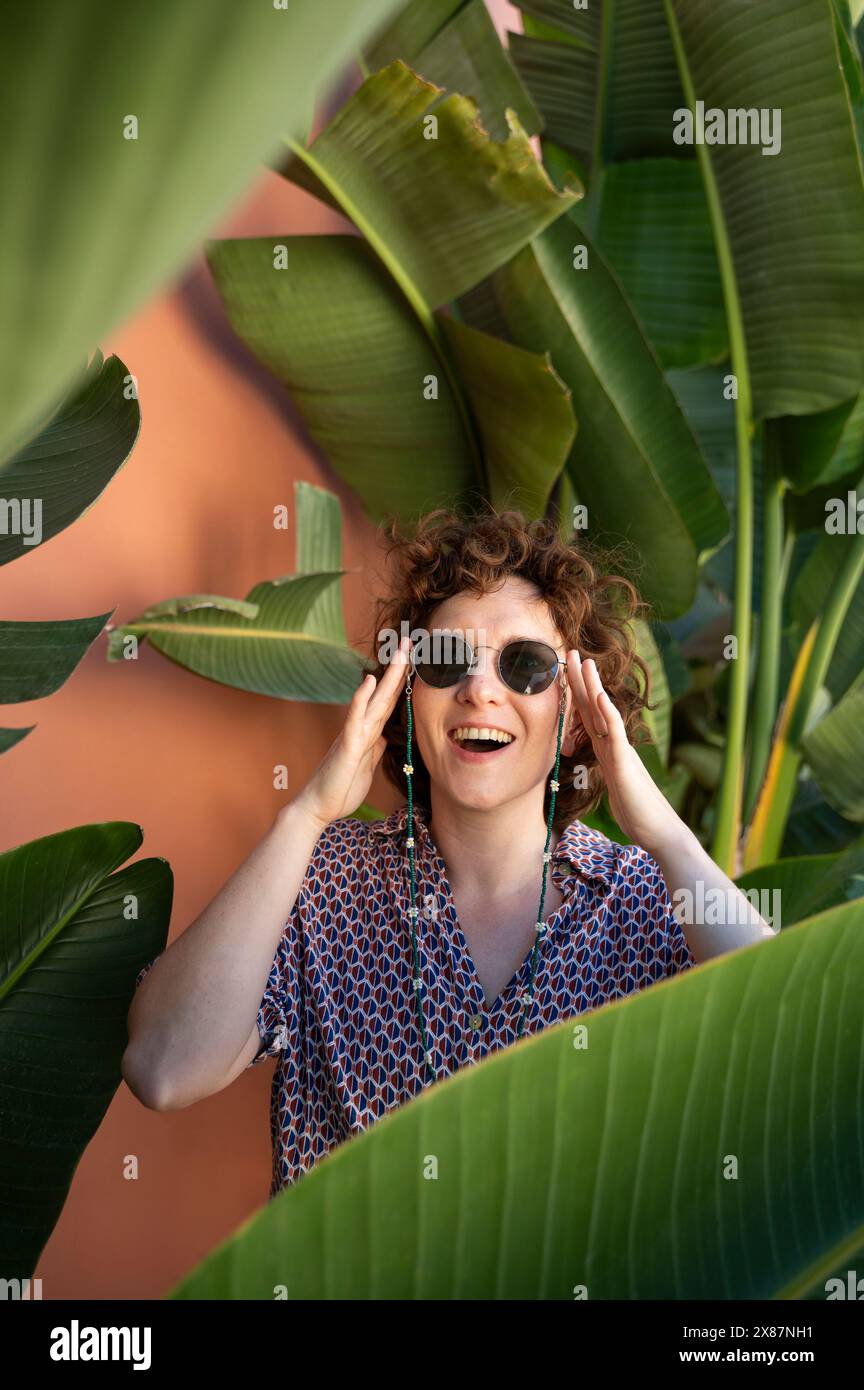 Femme à la mode portant des lunettes de soleil au milieu des palmiers Banque D'Images
