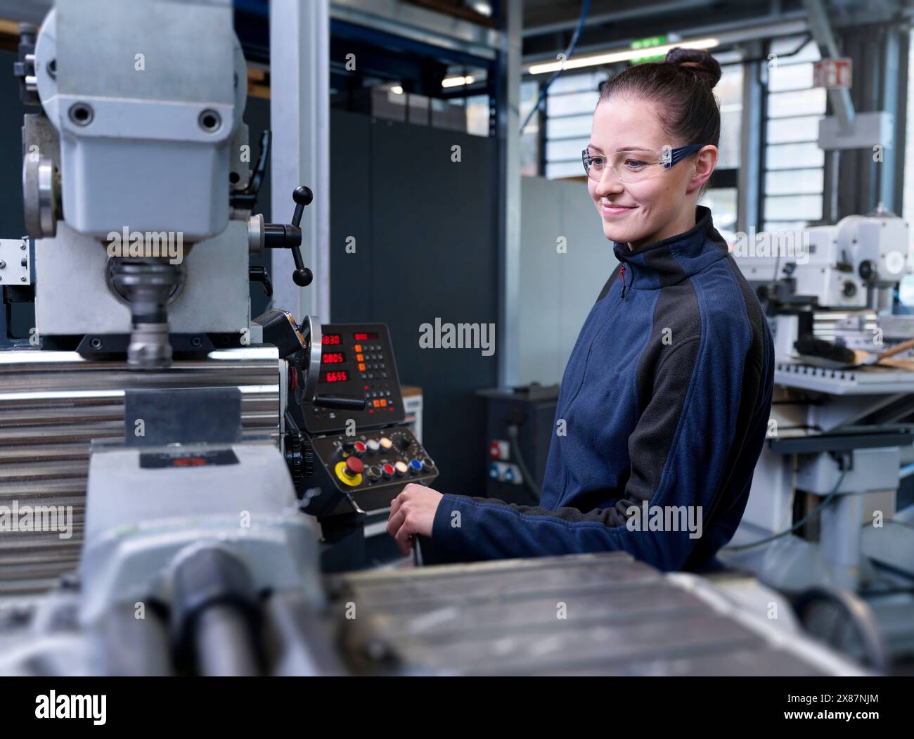 Ingénieur souriant avec des lunettes de protection actionnant la machine CNC à l'usine Banque D'Images