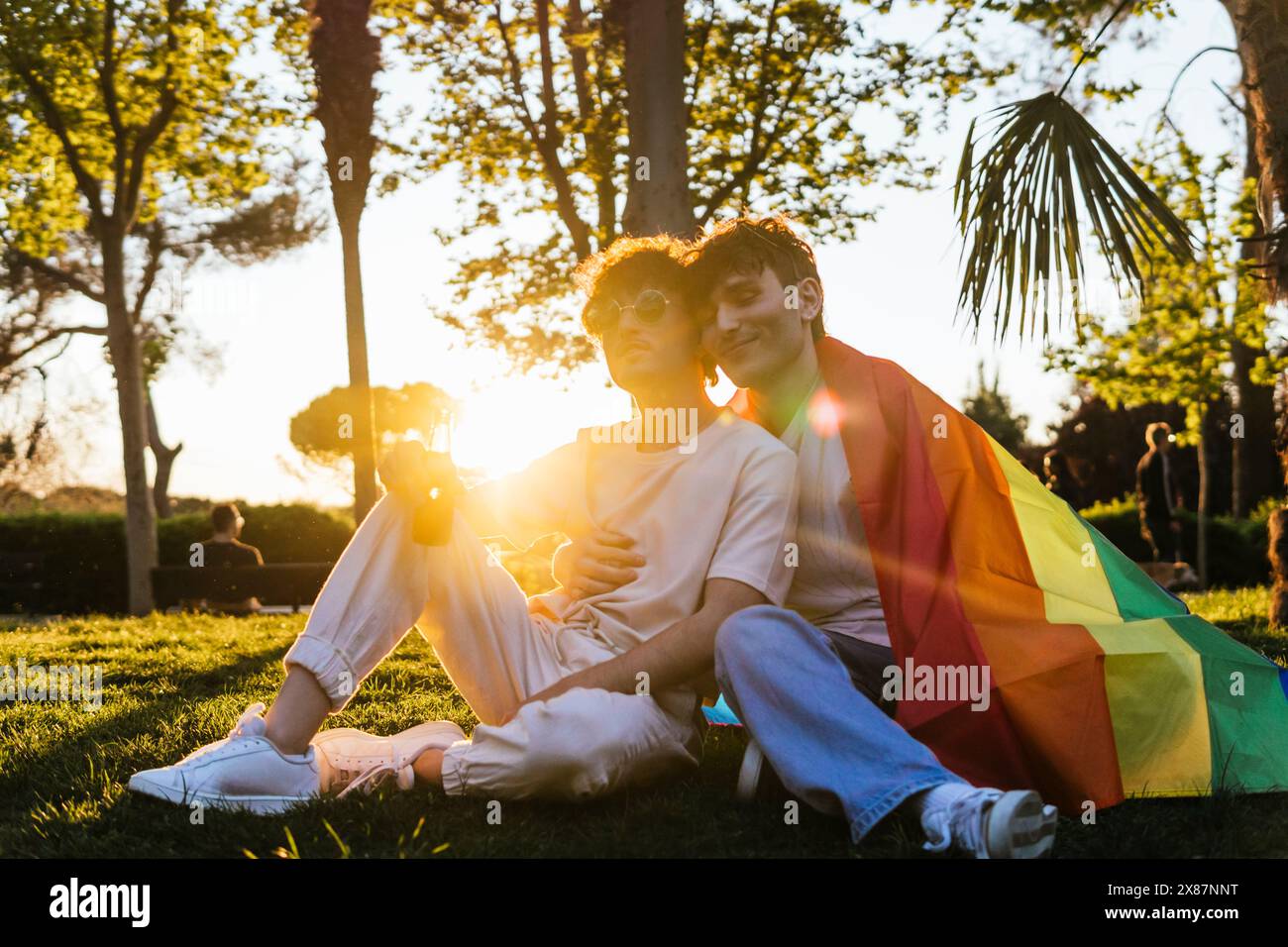 Jeune couple gay assis ensemble sur l'herbe au parc Banque D'Images