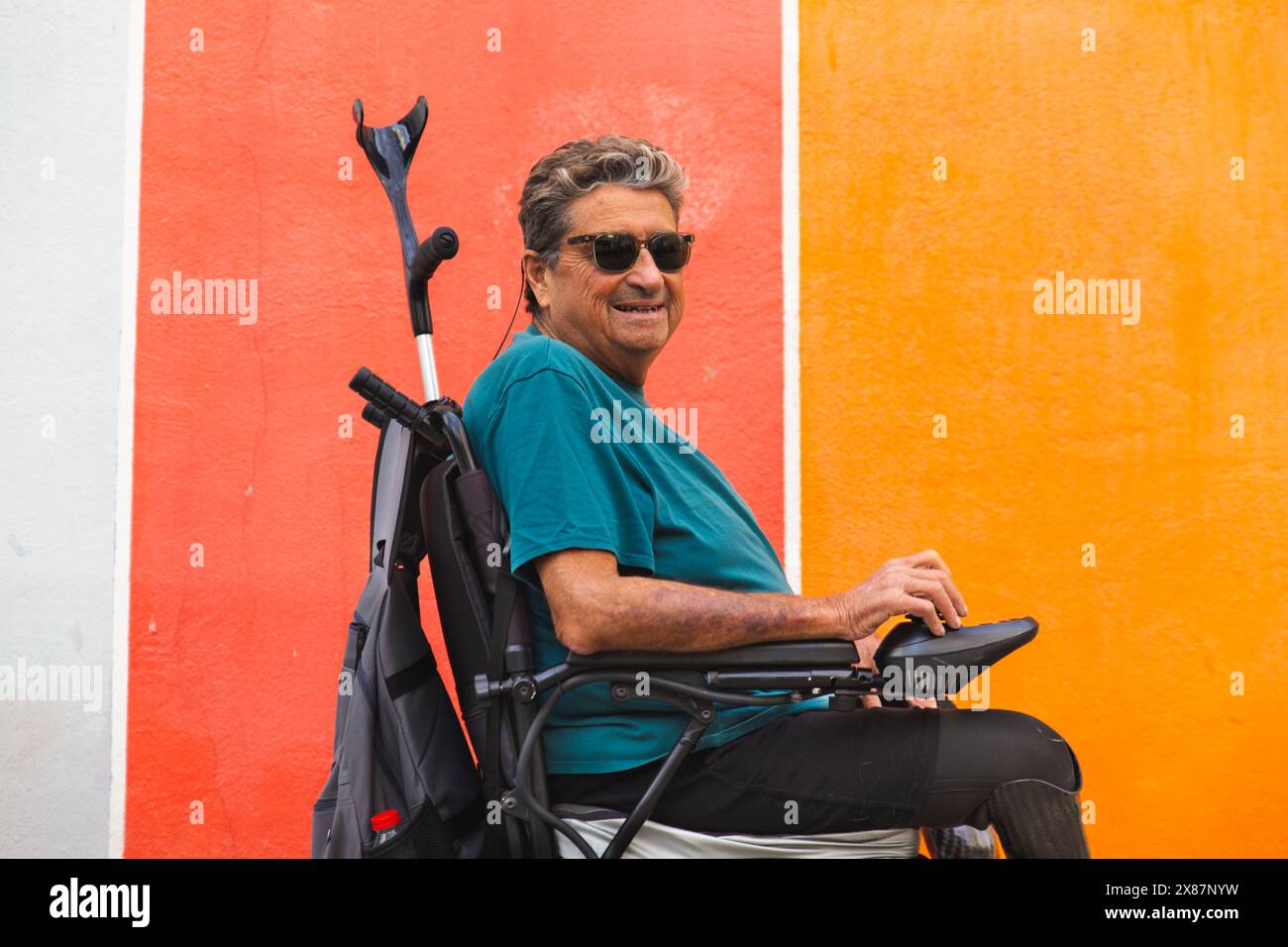 Homme senior retraité handicapé en fauteuil roulant motorisé par mur coloré Banque D'Images