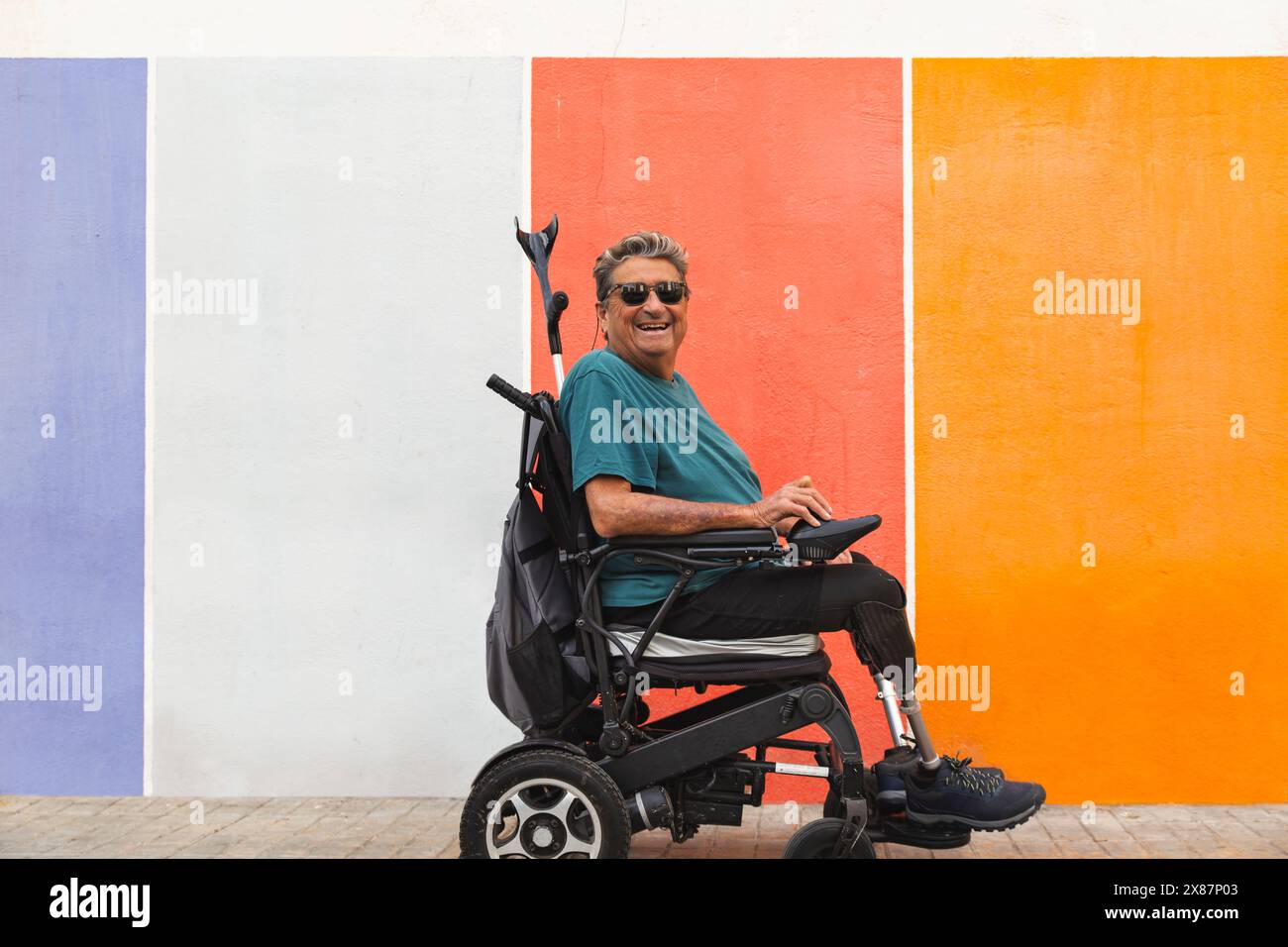 Homme senior heureux avec handicap en fauteuil roulant motorisé par mur coloré Banque D'Images