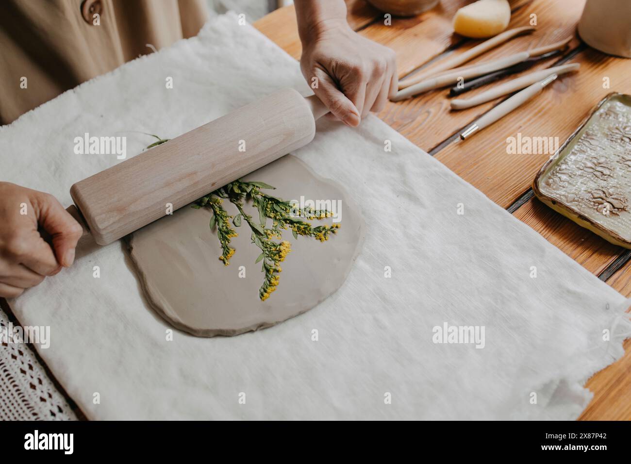 Mains de femme imprimant des fleurs sur de l'argile avec rouleau à pâtisserie à la maison Banque D'Images