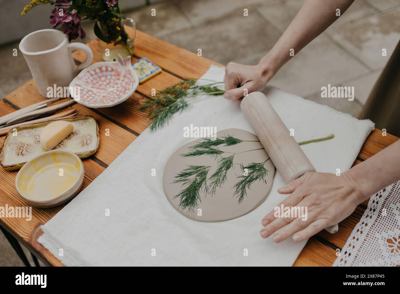 Mains de femme imprimant de l'herbe sur de l'argile avec rouleau à pâtisserie à la maison Banque D'Images Mains de femme imprimant de l'herbe sur de l'argile avec rouleau à pâtisserie à la maison Banque D'Images