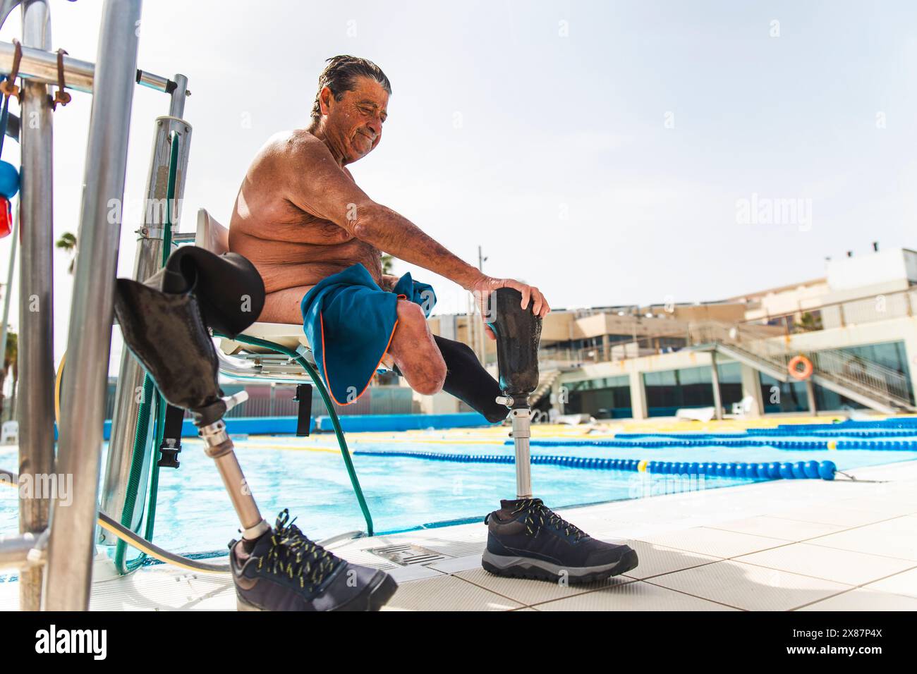 Homme âgé sans torse avec des jambes prothétiques assis sur une chaise hydraulique près de la piscine Banque D'Images Homme âgé sans torse avec des jambes prothétiques assis sur une chaise hydraulique près de la piscine Banque D'Images