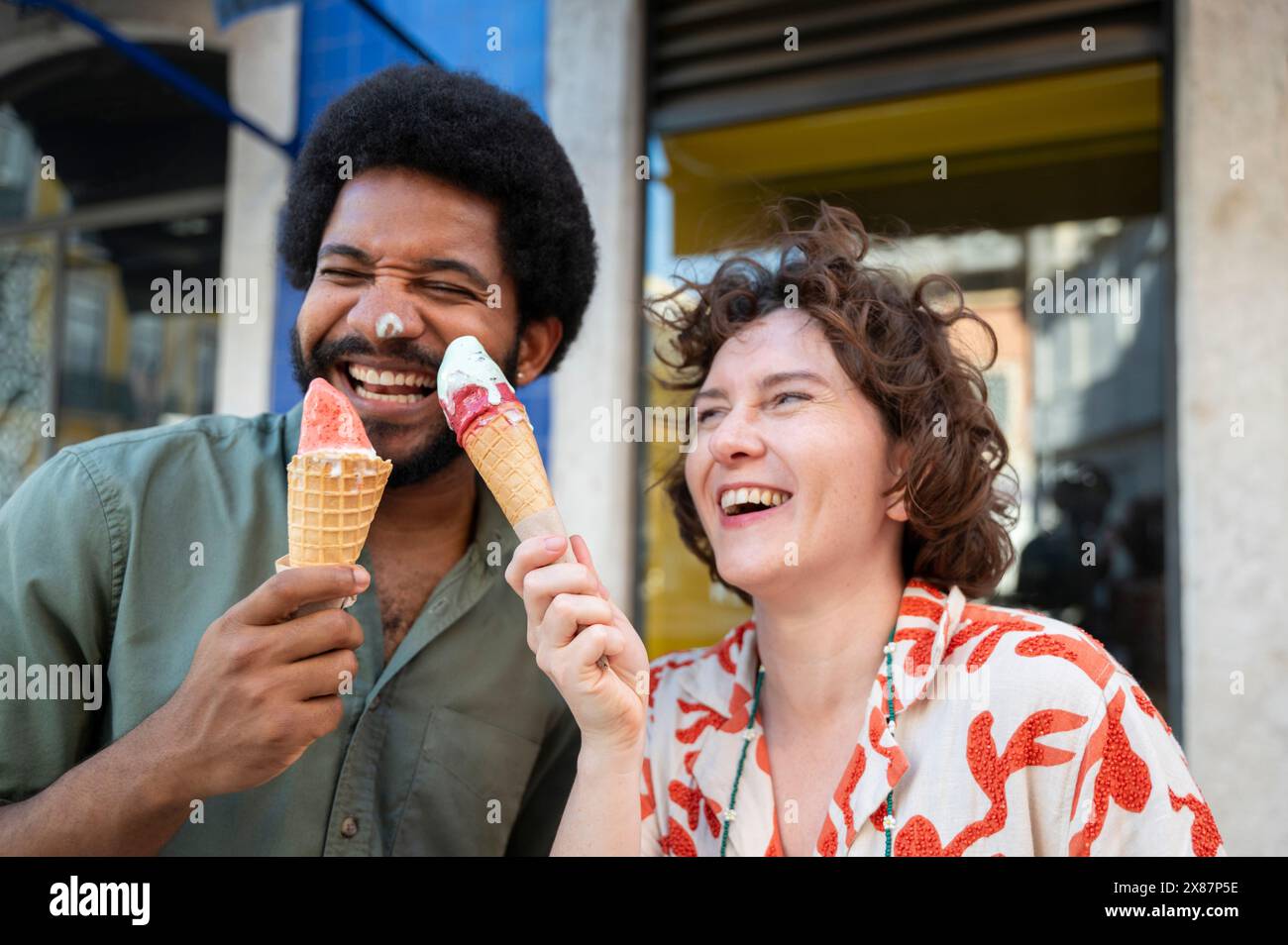 Couple joyeux s'amusant avec des cônes de crème glacée près du bâtiment Banque D'Images Couple joyeux s'amusant avec des cônes de crème glacée près du bâtiment Banque D'Images