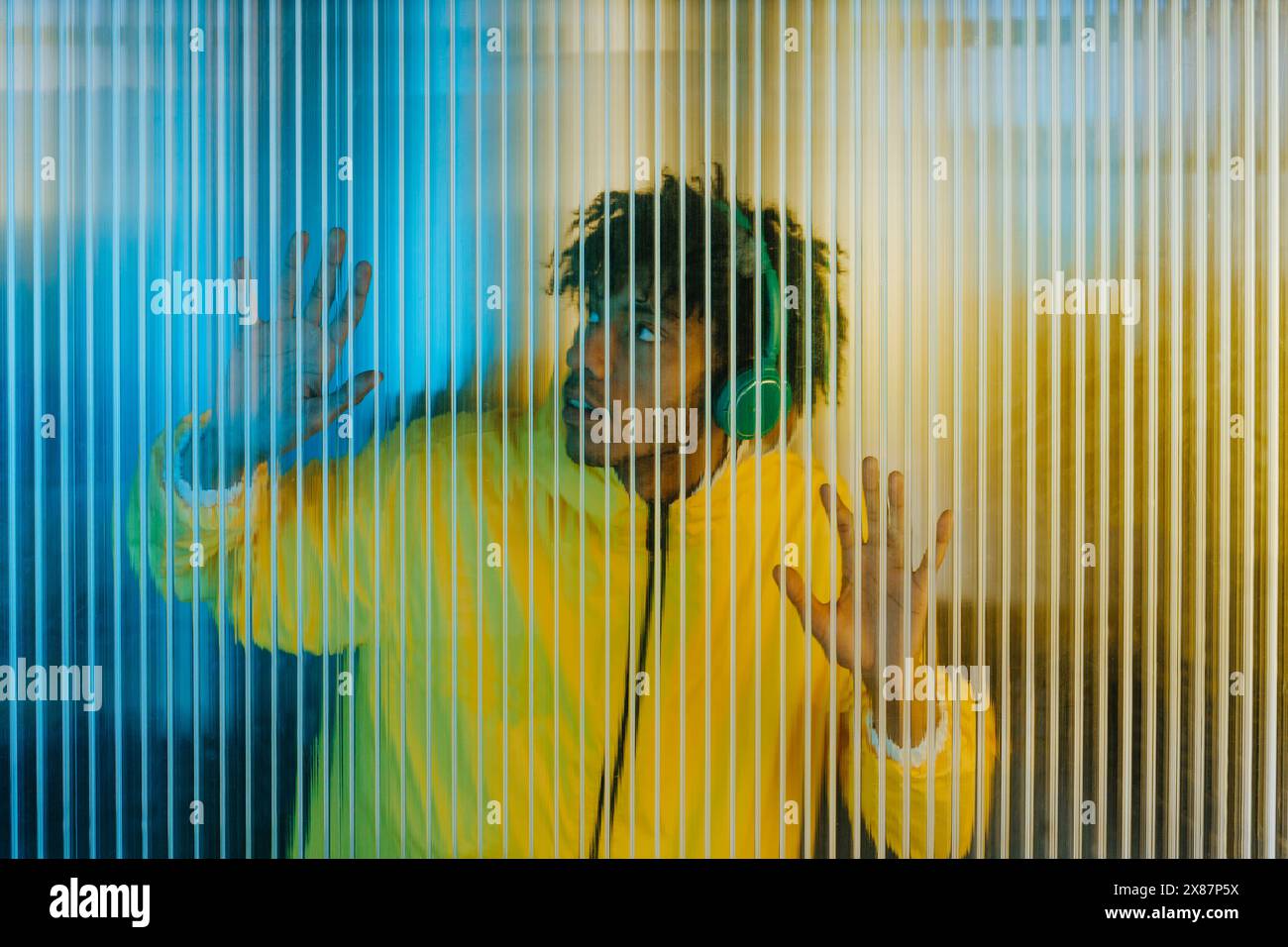 Jeune homme portant des écouteurs et écoutant de la musique près d'un mur rayé Banque D'Images Jeune homme portant des écouteurs et écoutant de la musique près d'un mur rayé Banque D'Images