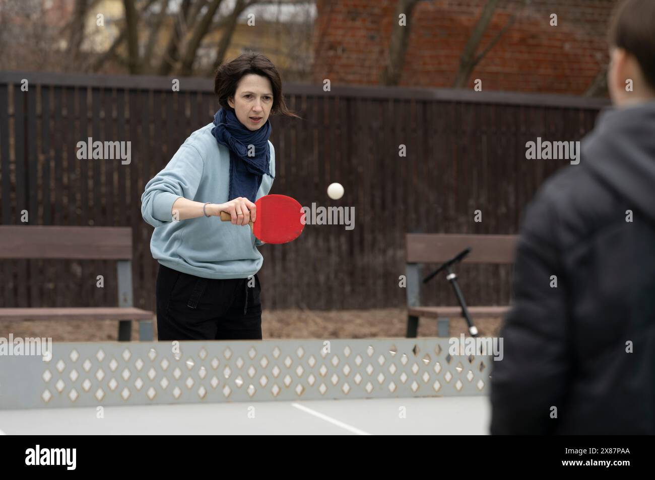 Femme jouant au tennis de table avec un garçon au parc public Banque D'Images Femme jouant au tennis de table avec un garçon au parc public Banque D'Images