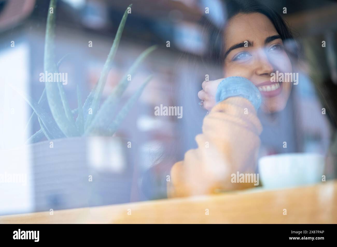 Femme souriante au café vu à travers la fenêtre de verre Banque D'Images