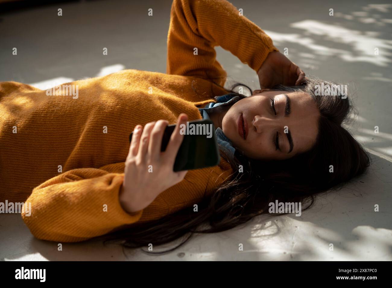 Femme avec la main dans les cheveux à l'aide d'un téléphone intelligent couché sur le sol à la maison Banque D'Images