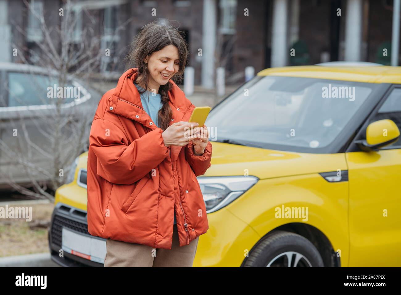 Femme souriante utilisant un téléphone intelligent debout à côté de la voiture jaune dans la rue Banque D'Images Femme souriante utilisant un téléphone intelligent debout à côté de la voiture jaune dans la rue Banque D'Images