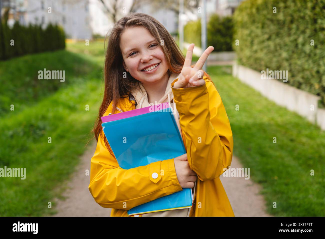 Fille souriante montrant le signe de paix et tenant des dossiers colorés Banque D'Images