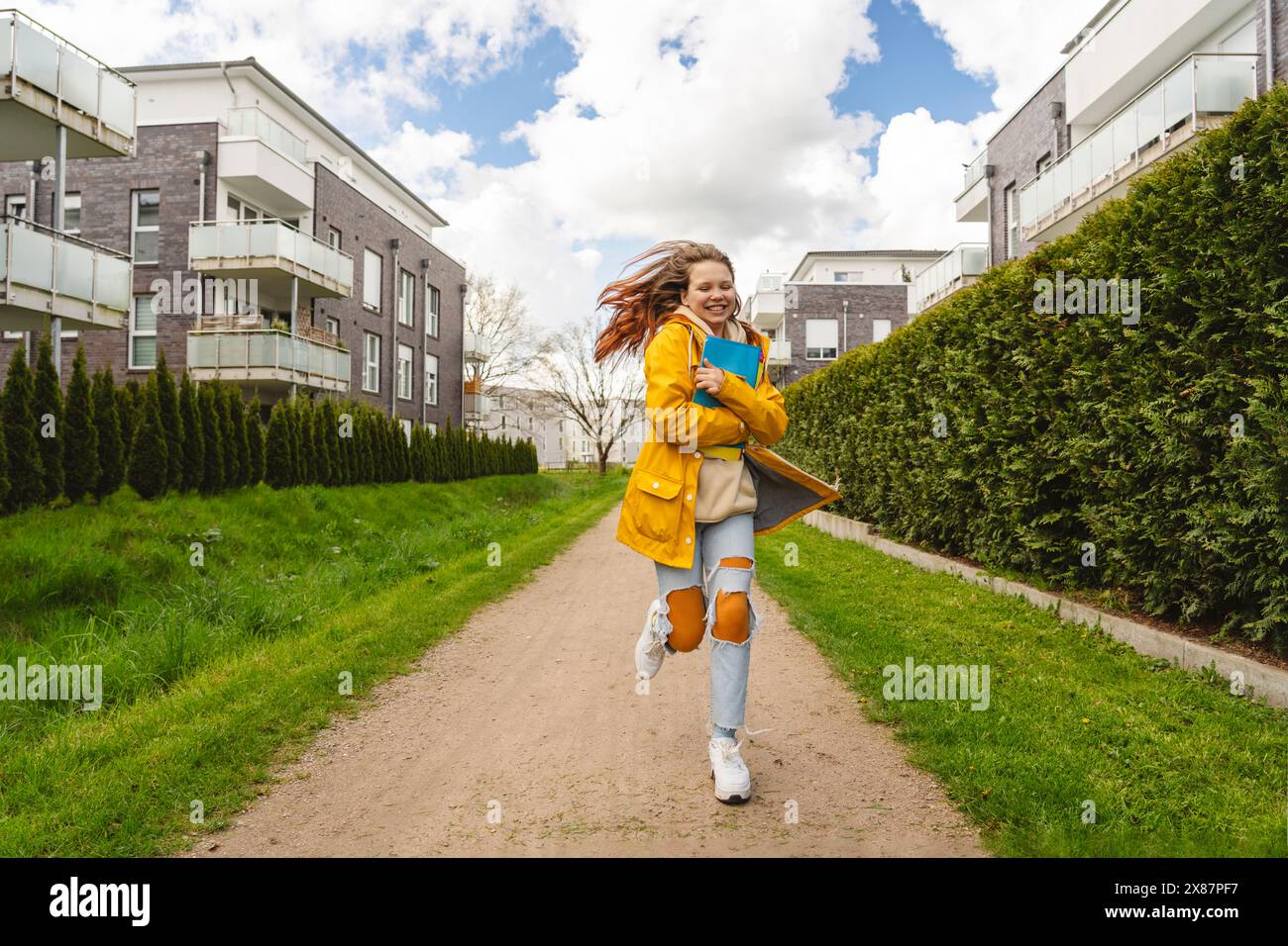 Jeune fille joyeuse courant avec des dossiers sur le sentier près des bâtiments Banque D'Images Jeune fille joyeuse courant avec des dossiers sur le sentier près des bâtiments Banque D'Images