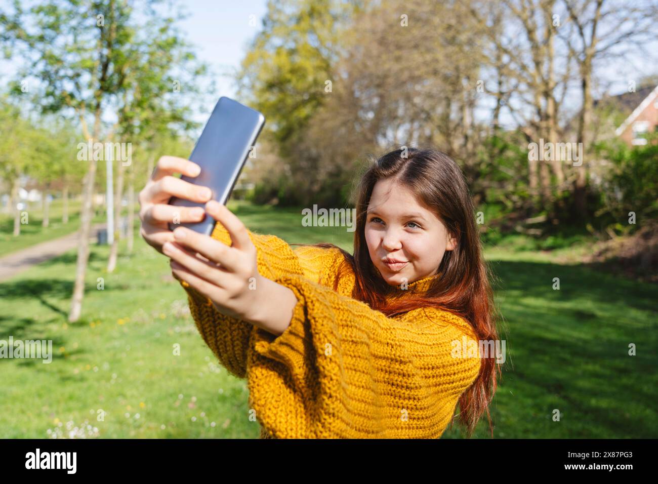 Fille souriante prenant selfie par téléphone intelligent au parc Banque D'Images