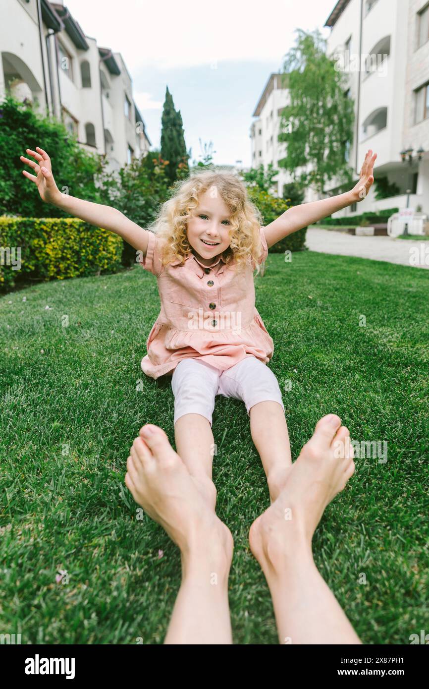 Fille souriante avec les bras levés assis sur l'herbe avec mère au parc Banque D'Images Fille souriante avec les bras levés assis sur l'herbe avec mère au parc Banque D'Images