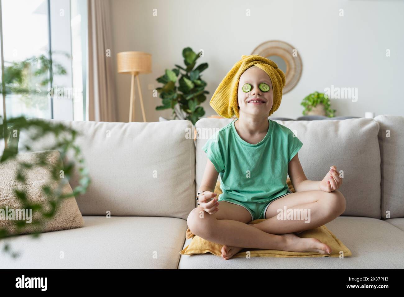 Fille souriante avec des tranches de concombre sur les yeux assis à la maison Banque D'Images Fille souriante avec des tranches de concombre sur les yeux assis à la maison Banque D'Images
