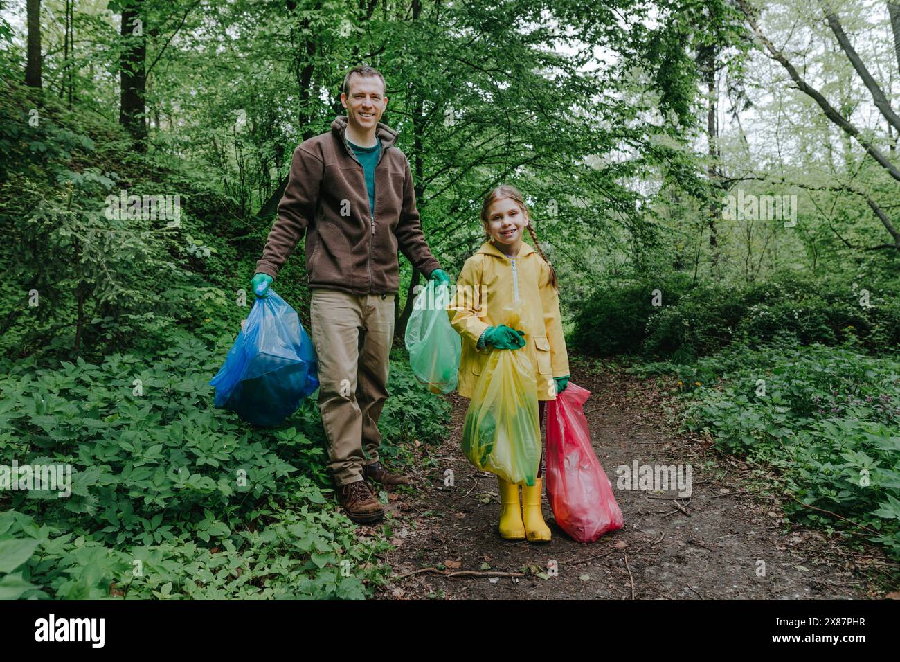 Heureux père et fille debout avec des sacs poubelles dans la forêt Banque D'Images