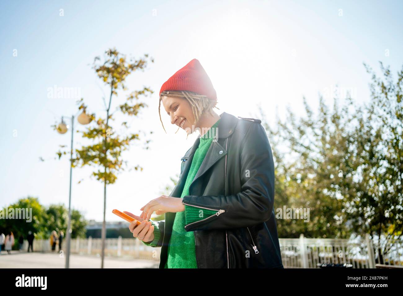 Jeune femme souriante utilisant un téléphone portable par beau temps Banque D'Images Jeune femme souriante utilisant un téléphone portable par beau temps Banque D'Images