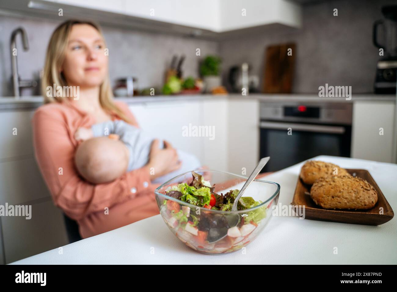 Nourriture fraîche sur la table à manger avec la mère allaitant son fils enfant en bas âge dans la cuisine Banque D'Images