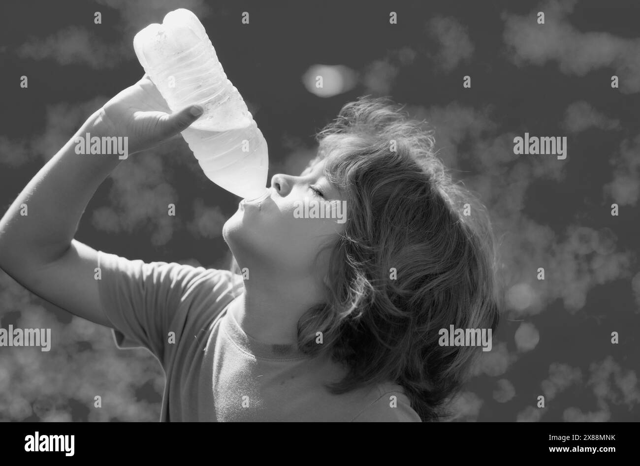 Enfant qui boit de l'eau douce. L'enfant tient un verre d'eau claire. Un mode de vie sain, des soins de santé. Un garçon en plein air boit une bouteille pure en verre. Gros plan Banque D'Images