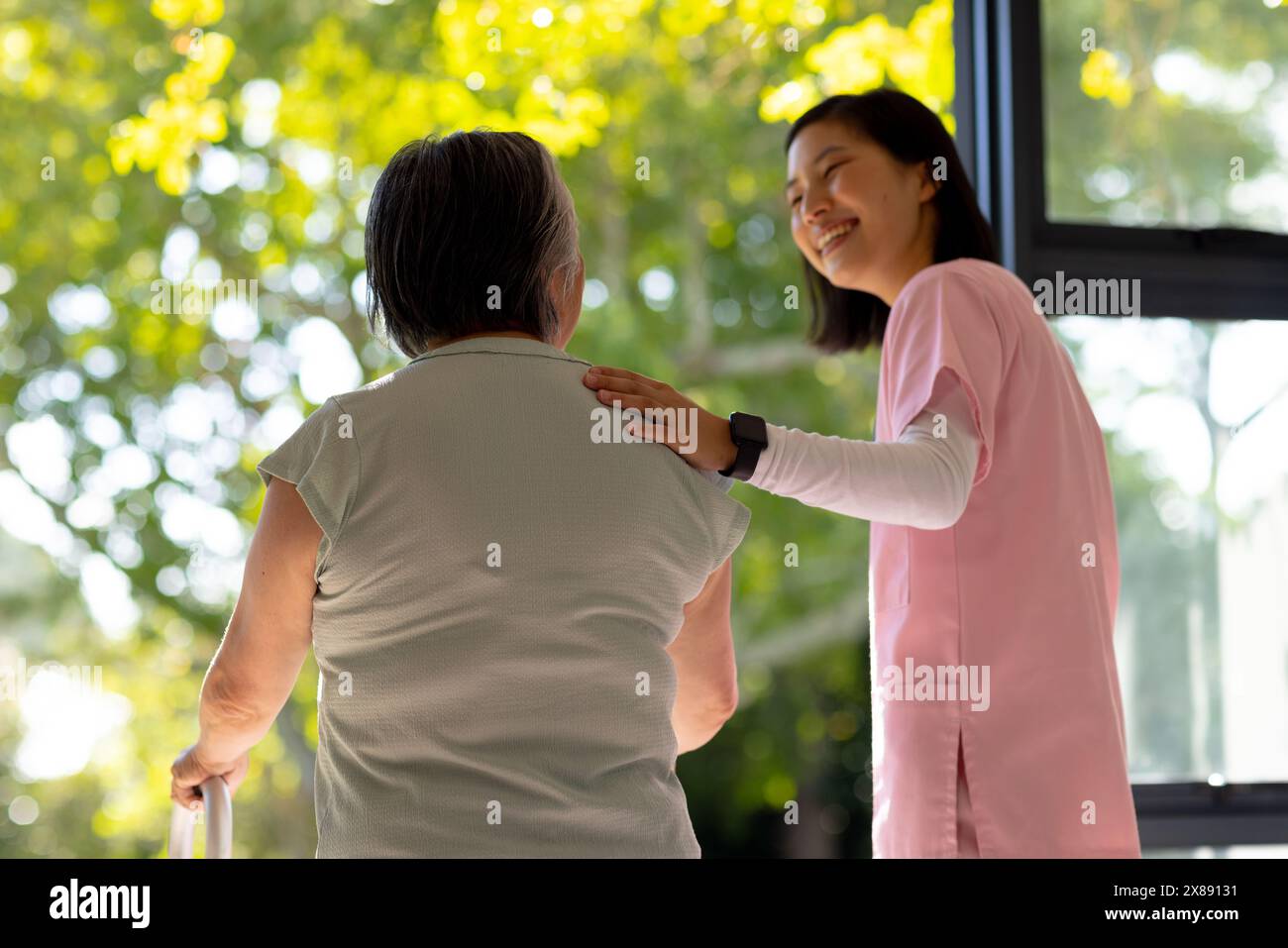 A la maison, jeune infirmière asiatique et patiente d'âge moyen, debout près de la fenêtre Banque D'Images