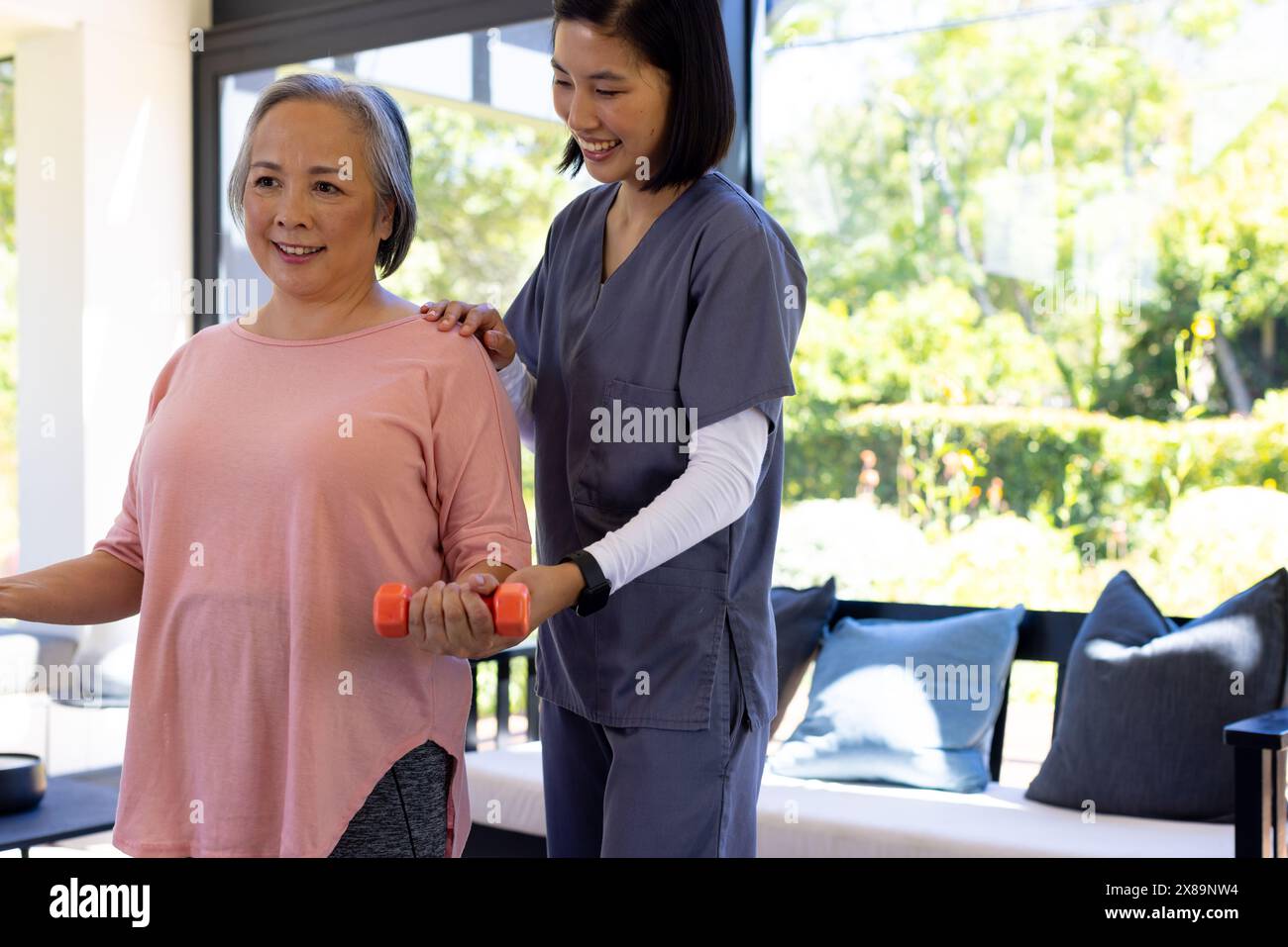 A domicile, jeune infirmière asiatique et patiente d'âge moyen pratiquant des exercices Banque D'Images