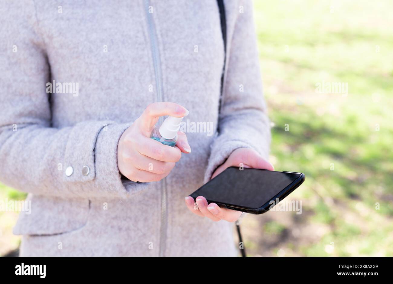 Gros plan sur la main d'une femme tenant son smartphone et nettoyant vaporisateur sur son smartphone. Bonnes pratiques d'hygiène personnelle dans la rue. Banque D'Images